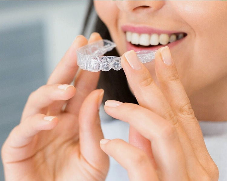 A smiling woman putting in her Invisalign clear aligners from her dentist in Centreville