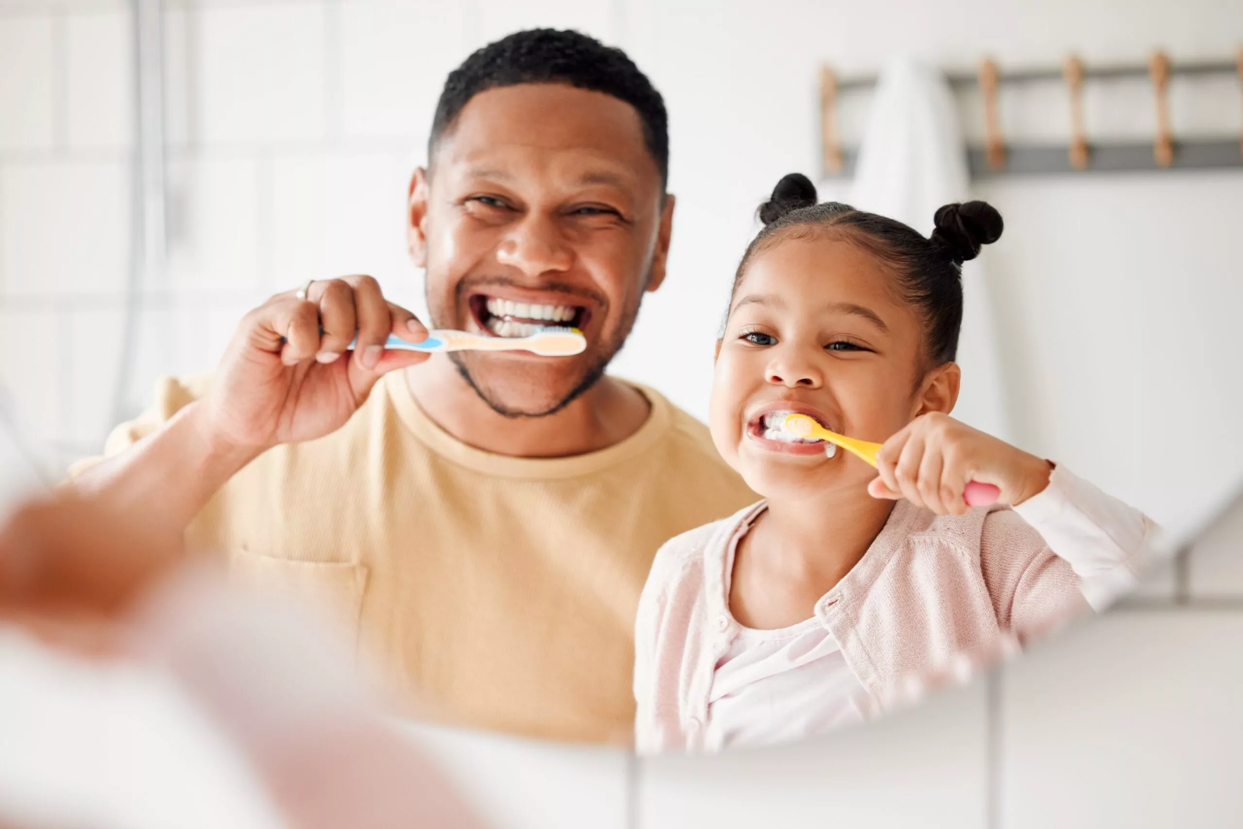 father and daughter brushing their teeth in the mirror, practicing proactive health care