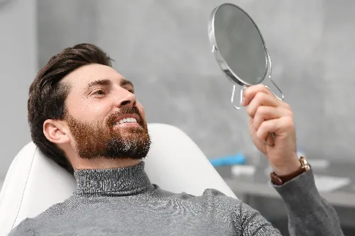 man smiling in a dental chair, looking in mirror, happy with new dental implants