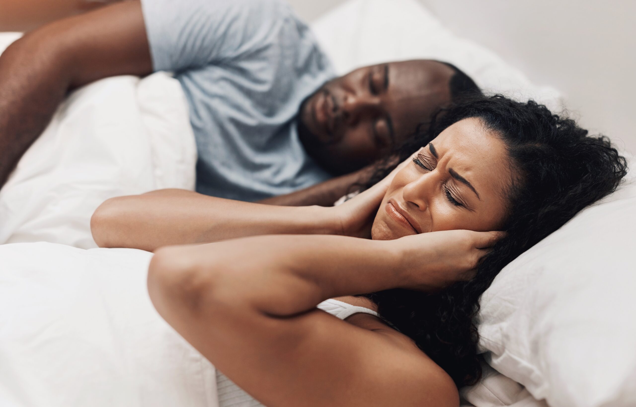 man snoring in bed next to partner who is covering her ears